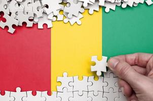 le drapeau de la guinée est représenté sur une table sur laquelle la main humaine plie un puzzle de couleur blanche photo