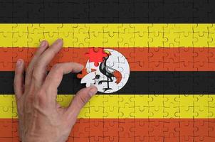 le drapeau de l'ouganda est représenté sur un puzzle, que la main de l'homme complète pour se plier photo