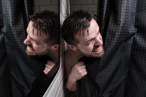 un homme mouillé regarde derrière un rideau de douche, regarde mal quelqu'un et montre ses dents. photo