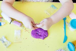 faire du slime à la maison. notion de bricolage. les mains font de la boue avec des paillettes sur fond jaune photo