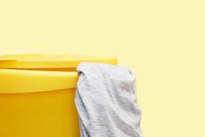 panier à linge en plastique jaune avec des vêtements gris sur fond jaune photo