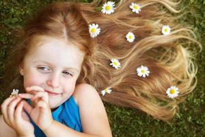 portrait d'une belle petite fille aux cheveux rouges en bonne santé avec des fleurs de camomille allongées sur l'herbe photo