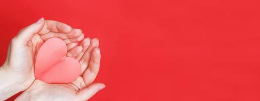 les mains féminines tiennent un coeur rouge sur les paumes isolées sur fond rouge. amour, mariage, saint valentin, concept du 8 mars. photo