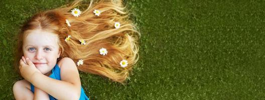 portrait d'une belle petite fille aux cheveux rouges en bonne santé avec des fleurs de camomille allongées sur l'herbe photo