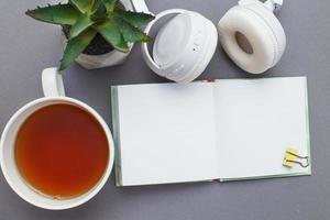 lieu de travail avec un bloc-notes, des écouteurs, une tasse de thé ou de café et une plante verte. espace de travail indépendant sur fond gris. photo