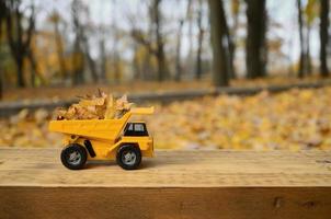 le concept de récolte saisonnière des feuilles mortes d'automne est représenté sous la forme d'un camion jouet jaune chargé de feuilles sur fond de parc d'automne photo