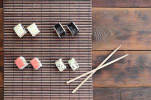 des rouleaux de sushi et des baguettes en bois reposent sur un tapis de couture en paille de bambou. cuisine asiatique traditionnelle. vue de dessus photo