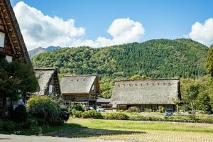 village japonais de shirakawago en octobre en automne saison des feuillages d'automne. maison traditionnelle de shirakawa sur un toit en triangle avec un arrière-plan de rizière, de montagne de pins et de ciel nuageux clair après. photo