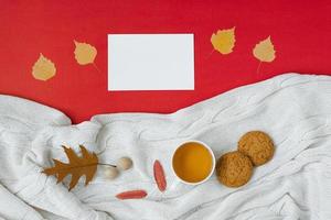 automne, le concept d'action de grâces. une tasse de thé, des feuilles d'automne tombées, une couverture tricotée, une feuille vierge blanche et propre pour le texte sur un fond rouge. espace de copie photo