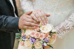 couple de jeunes mariés tenant un bouquet de roses. anneaux de mariage sur les mains de la mariée et du marié photo