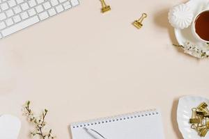 espace de travail de blogueur de beauté de mode avec clavier d'ordinateur portable, fleurs de pommier, tasse de thé, guimauve sur fond beige. mise à plat, vue de dessus, espace de copie photo