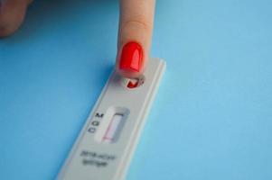 test pour le coronavirus sur fond bleu. une fille avec une manucure rouge vif fait un test sanguin pour déterminer les anticorps de classe igg et igm. Surveillance de la santé photo