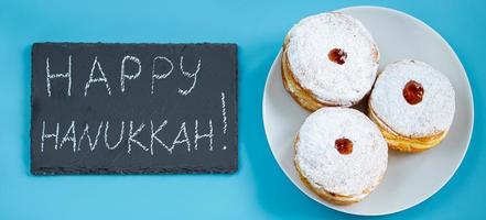 joyeux Hanoucca. dessert juif beignets sufganiyot sur fond bleu. symbole de la fête du judaïsme religieux. inscription au tableau noir. photo