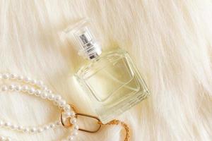 une bouteille transparente de produits cosmétiques repose sur une fourrure beige avec une longue pile et une décoration de perles. le concept de parfumerie et de beauté.