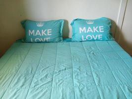 deux oreillers sur le lit dans la chambre blanche, la taie d'oreiller et le couvre-lit sont de couleur vert clair dans la chambre blanche. le mot blanc faire l'amour sur la taie d'oreiller. photo