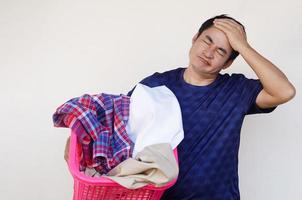 un homme asiatique tient un panier de tissu pour la lessive, se sent paresseux, ennuyé et fatigué, met la main sur la tête. concept, corvée quotidienne, travaux ménagers. l'homme ne veut pas laver les vêtements. faire une drôle de tête. photo
