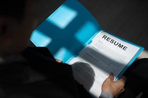 un chômeur postule pour un emploi assis dans la file d'attente tenant des documents de CV en attente d'un entretien d'embauche avec la lumière du soleil et l'ombre. photo