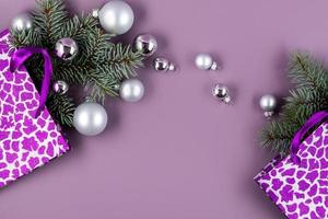 le concept d'un fond de noël. vue de dessus de boules d'argent d'une boîte-cadeau de noël avec des branches de sapin sur un fond violet à la mode. photo