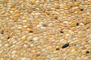 texture d'un mur de pierre, routes de petites pierres rondes et ovales avec du sable avec des coutures de vieux brun noir jaune naturel. l'arrière-plan photo