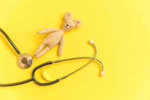 ours en peluche de conception simplement minimale et stéthoscope d'équipement de médecine isolé sur fond jaune. concept de médecin pour enfants de soins de santé. symbole du pédiatre. disposition de la vue de dessus à plat, espace de copie photo