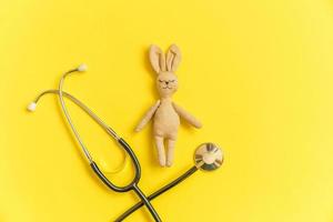 lapin jouet de conception simplement minimale et stéthoscope d'équipement médical isolé sur fond jaune. concept de médecin pour enfants de soins de santé. symbole du pédiatre. disposition de la vue de dessus à plat, espace de copie photo