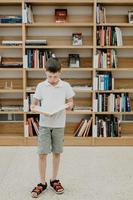 un garçon se tient dans la bibliothèque et lit un livre debout. préparation des devoirs. le garçon aime lire. espace libre à l'école. apprentissage extrascolaire. photo