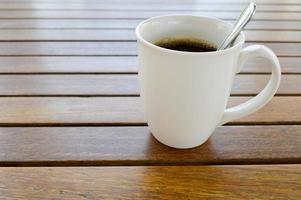 une tasse en céramique blanche avec un café chaud rafraîchissant le matin avec une boisson au thé et une cuillère à café brillante de thé est sur une table en bois dans un café photo