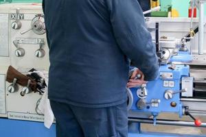 un travailleur masculin travaille sur un plus grand tour de serrurier en fer métallique, équipement de réparation, travail du métal dans un atelier d'une usine métallurgique dans une production de réparation photo