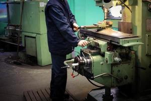 un travailleur masculin travaille sur un plus grand tour de serrurier en fer métallique, équipement de réparation, travail du métal dans un atelier d'une usine métallurgique dans une production de réparation photo