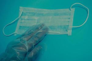 une main dans un gant en plastique tient un masque médical de protection jetable pour la protection contre les maladies mortelles dangereuses des microbes et des virus par le coronavirus covidum-19 sur fond bleu photo