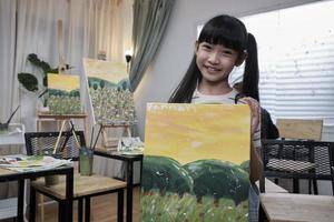 une étudiante asiatique montre son travail de peinture, fière d'un portfolio, d'une image couleur acrylique sur toile dans une salle de classe d'art et d'un apprentissage créatif avec des compétences de talent dans l'enseignement en studio de l'école primaire. photo