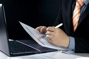 vue rapprochée de la main d'un homme d'affaires utilisant un stylo pour prendre des notes tout en travaillant sur un ordinateur portable au bureau photo