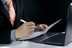 vue rapprochée de la main d'un homme d'affaires utilisant un stylo pour prendre des notes tout en travaillant sur un ordinateur portable au bureau photo