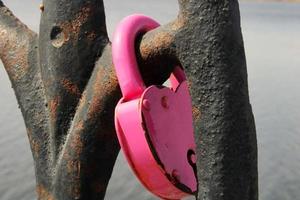 un cadenas rose en forme de gros plan de coeur est suspendu à un treillis rouillé. tradition du mariage. le concept de l'amour et de la fidélité photo