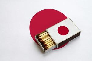 le drapeau du japon est affiché dans une boîte d'allumettes ouverte, qui est remplie d'allumettes et repose sur un grand drapeau photo