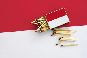 le drapeau indonésien est affiché sur une boîte d'allumettes ouverte, d'où tombent plusieurs allumettes et repose sur un grand drapeau photo