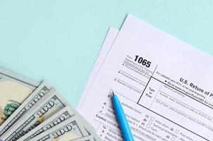 Le formulaire d'impôt 1065 se trouve près de cent billets d'un dollar et d'un stylo bleu sur fond bleu clair. nous retour pour le revenu parental photo