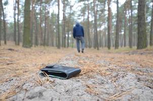 jeune homme perd son sac à main avec des billets en euros sur le chemin du bois de sapin d'automne russe. insouciance et perte de concept de portefeuille photo