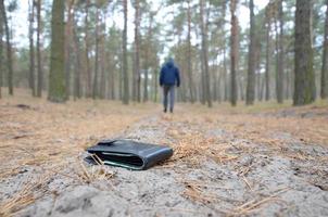 jeune homme perd son sac à main avec des billets en euros sur le chemin du bois de sapin d'automne russe. insouciance et perte de concept de portefeuille photo