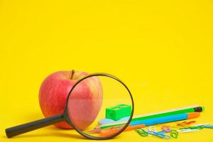 pomme, loupe et fond jaune de papeterie scolaire. photo