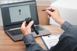 Main un homme tient l'ancien moteur à essence de bougie d'allumage de bobine et l'ordinateur portable vérifie l'exactitude des pièces de rechange avant de les retirer du concept de bureau de service de voiture de stock photo