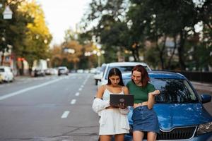 deux jeunes femmes avec un ordinateur portable près de la voiture photo