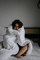 femme paresseuse enveloppée dans une couverture douce assise dans un lit douillet photo