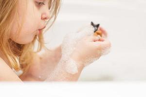 petite fille aux cheveux blonds jouant avec de la mousse dans une baignoire. fille prend un bain. fille jouant avec des jouets dans le bain photo