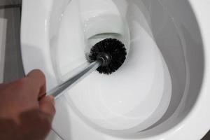 la main nettoie une cuvette de toilette blanche avec une brosse. tâches ménagères. vue de dessus. fermer. photo