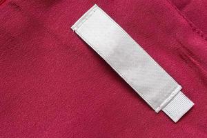 étiquette de vêtements de soin de lessive blanche vierge sur fond de texture de tissu rouge photo