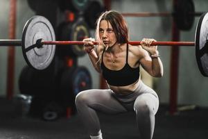 femme musclée faisant des exercices de squat avec des haltères à la salle de gym photo