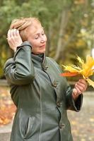 une femme âgée dans un parc d'automne recueille un bouquet de feuilles d'érable jaunes. photo
