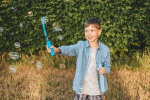 un garçon joue avec des bulles de savon dans un parc d'été, parmi la verdure. photo