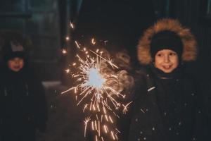 garçon tient un cierge magique dans ses mains tout en célébrant une nouvelle année dans la rue la nuit. feux d'artifice entre les mains des enfants lors de la célébration du nouvel an. photo